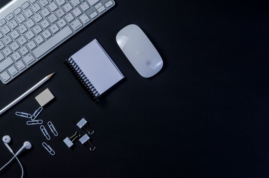 Flat lay of a modern workspace with keyboard, mouse, and stationery on a dark background.
